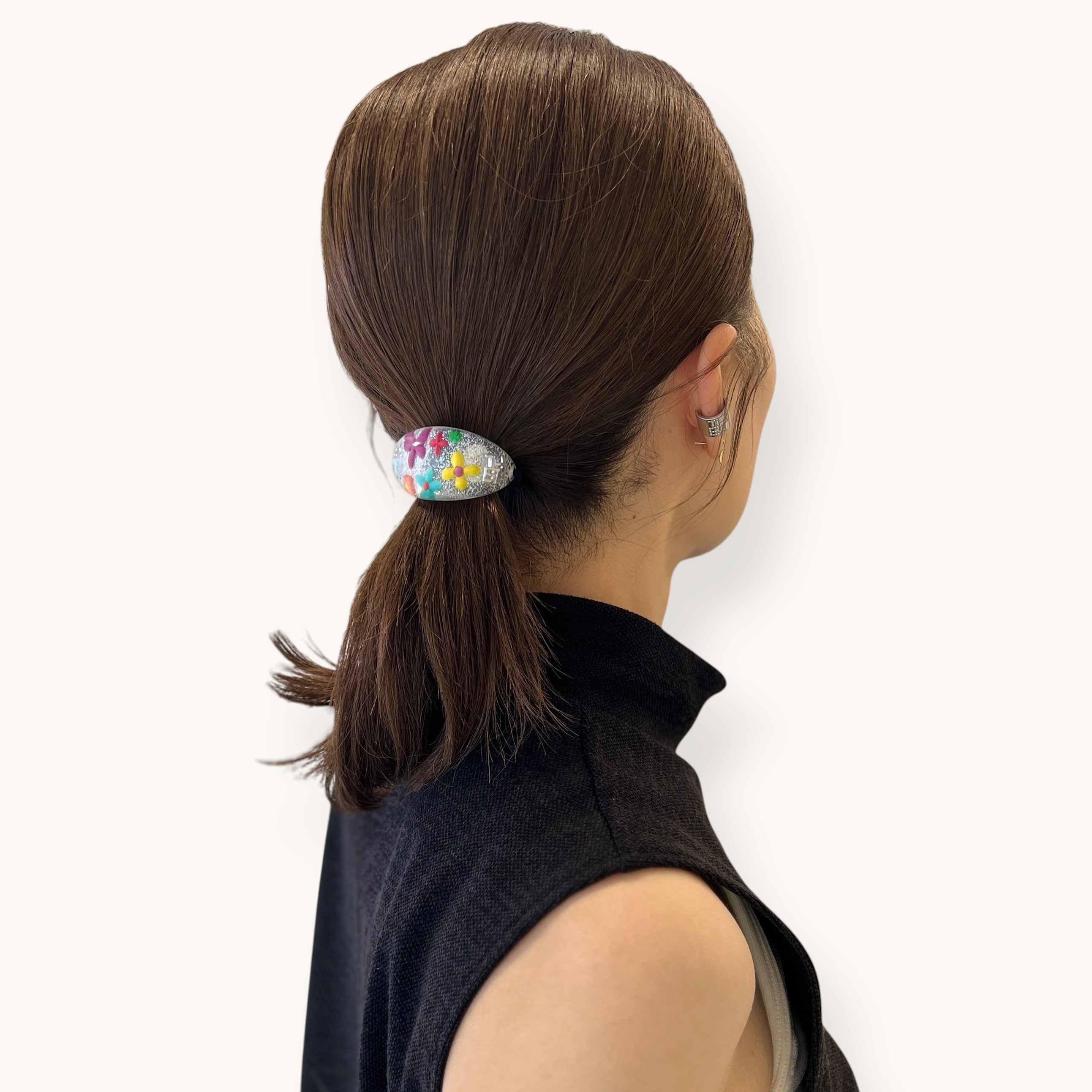 THE HAIR BAR TOKYOのオーバル型ポニー。クリアなルーサイト素材に花と蝶、ラメを閉じ込めた華やかなヘアアクセサリーを着用した女性のヘアスタイル。